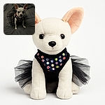 A tiny white Chihuahua wearing a sparkly black tutu dress sits on a dark gray quilted blanket, looking straight at the camera with big curious eyes and perky ears, ready for a night of fancy fun.