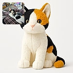 A charming calico kitten lounges comfortably on a person's plaid-clad lap, gazing curiously at the camera with wide, innocent eyes. The cozy indoor setting is filled with scattered toys and furniture, adding to the relaxed and homely vibe.