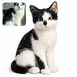 A charming black-and-white cat sits gracefully on a soft surface, looking directly at the camera with curious eyes. The background features a decorative wall piece with circular mirrors, adding an artistic touch to the cozy indoor setting.