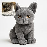 A curious gray kitten lounges on a soft, fuzzy cat tree platform, peeking out with alert eyes and delicate paws tucked beneath its body, basking in warm indoor light with a cozy kitchen background.