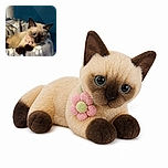 A tiny Siamese kitten lounges like a plush-bedded monarch, wearing a flower collar and giving the camera a wonderfully serious stare while its paws drape over the fuzzy blanket throne.
