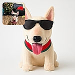 A cool white dog wearing sunglasses and a festive sweater stands on a wooden floor with a decorated Christmas tree and cozy furniture in the background, looking like the ultimate holiday party guest.