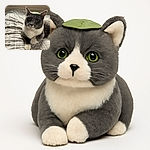A charming gray and white cat lounges on a patterned bedspread with a small green leaf perfectly balanced on its head, looking curiously at the camera. The cozy room background includes potted plants on a windowsill, adding a touch of nature to this adorable moment.