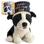 A joyful dog wearing a festive 'Happy New Year 2026' hat looks up with a big smile, capturing the excitement of ringing in the new year. The warm wooden floor and blurred background add a cozy, celebratory vibe.