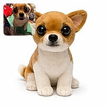 A tiny, wide-eyed Chihuahua stands on a cluttered bed, looking curiously at the camera with its tail wagging in excitement. The background is a cozy mess of blankets and clothes, making the dog the undeniable star of this candid snapshot.