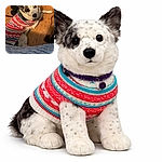 A spotted pup in a colorful holiday sweater looks up with an adorably guilty 'did I do that?' expression while lounging on a warm wooden floor next to shoes and a quilt — equal parts cozy and mischievous.