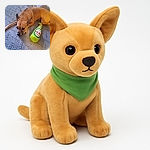 A small tan dog lies on a patterned blanket looking thoughtfully to the side, next to a bright green plush toy shaped like a beer bottle labeled 'Dos Patas Cerveza'. The cozy setting and the dog's calm expression make for a charming, casual snapshot.