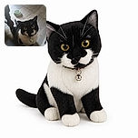 A wide-eyed tuxedo cat gazes up at the camera like it has just been appointed supervisor of the entire dining room. Its tiny bell adds an official touch, while an empty bowl waits nearby for the next snack inspection.
