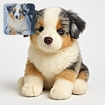 A fluffy, tricolor Australian Shepherd puppy lounges on a tiled floor, looking curiously at the camera with soft, soulful eyes and a nose with charming pink spots, while a black fabric object is partially visible on the right.