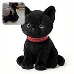 A playful black kitten with a red collar is lying on the floor, grabbing a large plush toy shaped like a bird wearing a black hat with a red band. The background shows a patterned curtain and a red ball toy on the floor.