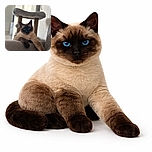 A majestic Siamese cat lounges casually on a gray couch, one paw stretched out like it owns the place. Behind it, a cozy cat tree stands blurred, adding depth and a hint of feline luxury to this perfectly focused portrait.