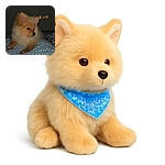 A fluffy, golden Pomeranian puppy lounges on a patterned blue and white bedspread, looking off to the side with a calm expression. The background is dark, highlighting the soft fur and cozy setting. A cute teddy bear, sparkle, and heart emoji float near the puppy's head, adding a playful touch.