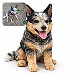 A happy dog with a speckled coat sits on a patch of dirt and leaves, panting with its tongue out as if it just finished a playful romp. The rustic wooden fence and scattered greenery in the background add a cozy outdoor vibe.