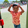 Isaac a rejoint le concours — aidez-le/la à gagner de superbes lots ! toddler, child, cap, hat, orange_shirt, denim_shorts, sneakers, playground, outdoor, daylight, people, kids, adults, fence, trees, blue_sky, curious, standing, expression, sunny