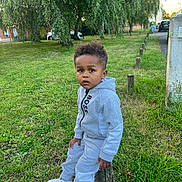 Isaac a rejoint le concours — aidez-le/la à gagner de superbes lots ! child, toddler, grass, tree, park, outdoor, sneakers, clothing, hoodie, pants, post, greenery, daylight, casual, curly_hair, person, nature, urban, sidewalk, expression