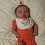 baby, bed, bib, bow, child, cute, expression, face, hand, head, indoor, infant, lying_down, onesie, orange_clothing, person, portrait, pout, quilt, skin