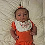 baby, bib, child, cute, expression, face, hair_tie, indoor, infant, lying_down, newborn, onesie, orange_clothing, person, pink_bow, portrait, pout, quilted_blanket, small_hands, soft_lighting