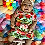 Valentina is registered to the contest to win money with this photo: baby, infant, smile, bow, floral_dress, colorful_blanket, soft_toys, plush, cute, happy, lying_down, indoors, child, adorable, pink_booties, headwear, face, skin, person, cozy