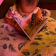 Valentina is registered to the contest to win money with this photo: baby, book, carpet, child, curious, cushion, elmo, floor, hand, head, indoor, leaf_pattern, onesie, pacifier, pink, play_gym, reading, seated, soft_toys, toy