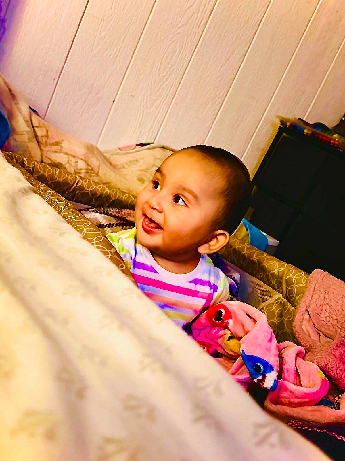 Valentina is registered to the contest to win money with this photo: baby, child, smiling, indoor, blanket, plush_toy, colorful_clothing, face, person, bedroom, furniture, wooden_wall, comfort, cute, happy, infant, toy, soft, cozy, portrait