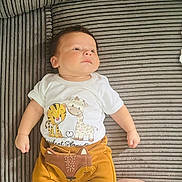 Riley is registered to the contest to win money with this photo: baby, infant, child, couch, striped_couch, white_shirt, cartoon_animals, mustard_pants, fox_design, socks, yellow_socks, person, legs, lace_clothing, resting, indoor, portrait, cute, lying_down, looking_away