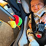 baby, car_seat, smile, infant, toy, plush, seatbelt, clothing, sock, indoor, child, person, happy, caterpillar_toy, fabric, head_support, baby_clothes, safety_harness, car_seat_padding, floor