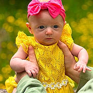 Willow joined the competition — help win amazing prizes! baby, infant, yellow_dress, pink_bow, headband, hands, portrait, outdoor, flowers, greenery, cute, child, human, person, summer, nature, soft_focus, colorful, closeup, holding