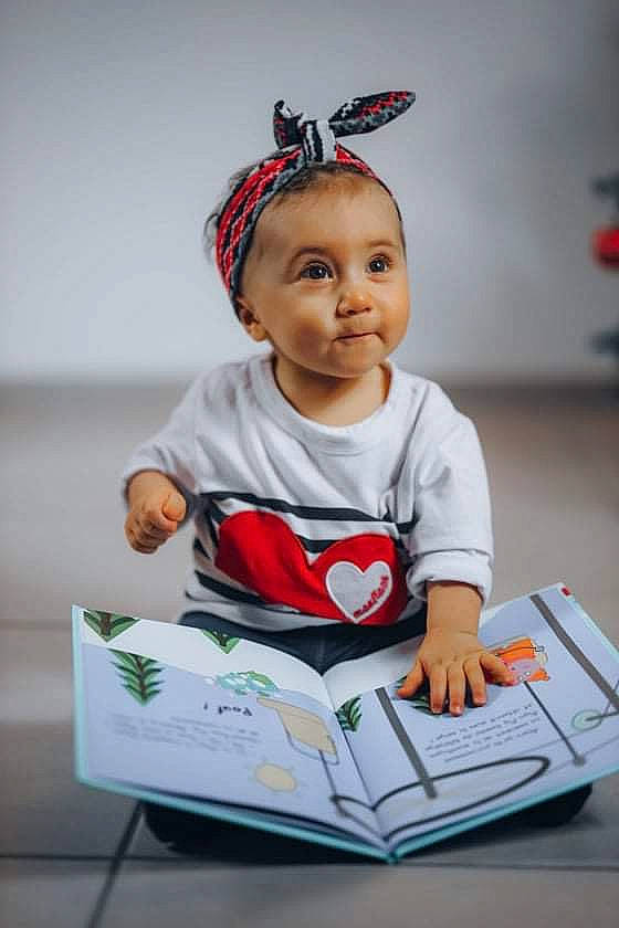 Ambre a rejoint le concours — aidez-le/la à gagner de superbes lots ! baby, baby_toddler_clothing, book, carmine, child, costume_hat, eye, fashion_accessory, fun, happy, person, portrait_photography, reading, room, sitting, sleeve, smile, t_shirt, toddler