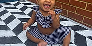 Brielle is registered to the contest to win money with this photo: baby, child, smiling, laughing, sitting, outdoor, brick_wall, black_and_white, checkered_clothing, patterned_rug, barefoot, cute, happy, infant, person, head, face, apparel, playful, young