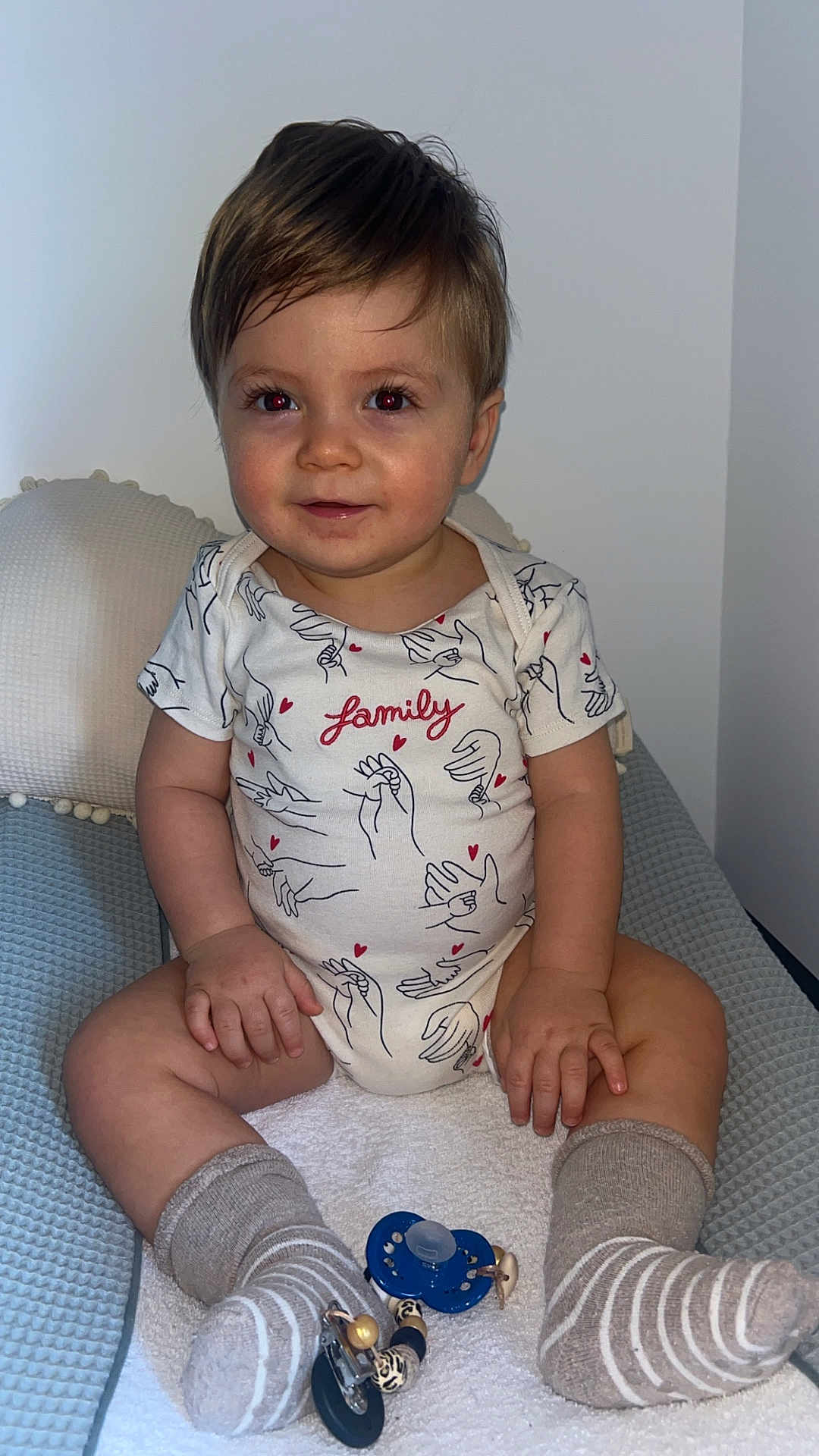 Romeo a rejoint le concours — aidez-le/la à gagner de superbes lots ! child, baby, toddler, sitting, onesie, printed_onesie, family_word, short_hair, smile, red_eye, pillow, cushion, blanket, socks, pacifier, pacifier_clip, hands, legs, indoor, portrait