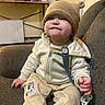 Ja Vonte is registered to the contest to win money with this photo: baby, child, smiling, hat, beige_clothing, jacket, pants, socks, indoor, couch, furniture, toy, mickey_mouse, photograph, mug, shelf, face, person, cute, happy