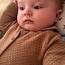 baby, child, face, portrait, sweater, brown_clothing, indoor, blanket, pillow, soft_texture, star_pattern, cute, infant, young_child, resting, cozy, warm, skin, head, expression