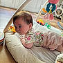 baby, infant, play_mat, toy, plush_toy, floor, window, sunlight, indoor, child, clothing, shorts, patterned_shirt, crawling, curious, soft_toy, colorful, play_area, tiled_floor, home