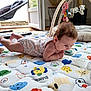 baby, infant, play_mat, toy, onesie, floor, indoor, child, cute, colorful, plush_toys, baby_gym, curious, crawling, soft_mattress, patterned, animal_prints, wooden_floor, open_door, natural_light