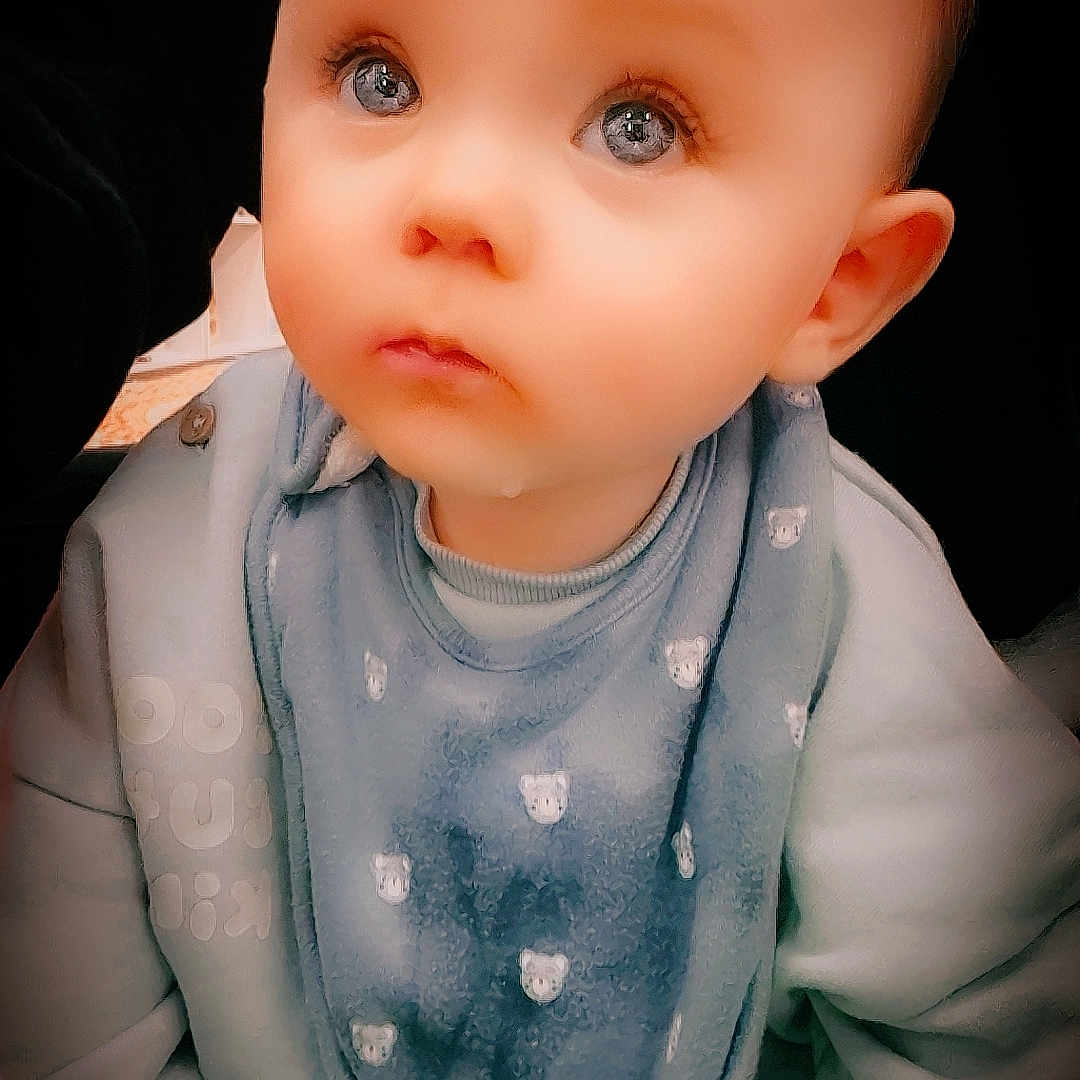 Orsen Rex is registered to the contest to win money with this photo: baby, bib, blue_clothing, child, cozy, cute, expression, eyes, face, hands, head, indoors, infant, looking_up, person, portrait, sitting, skin, soft_lighting, young_child