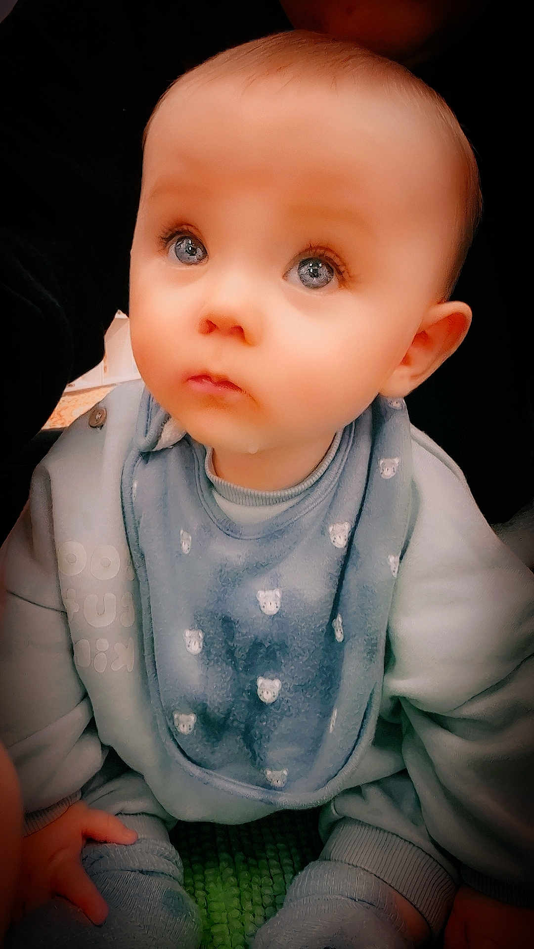 Orsen Rex is registered to the contest to win money with this photo: baby, child, blue_clothing, bib, cute, infant, indoors, looking_up, person, sitting, soft_lighting, young_child, cozy, hands, face, eyes, expression, skin, head, portrait