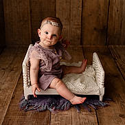 Joelle is registered to the contest to win money with this photo: armchair, baby, bodypart, chair, clothing, couch, doll, dress, face, finger, furniture, hand, hardwood, head, person, photography, portrait, sitting, toy, wood