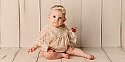 Joelle is registered to the contest to win money with this photo: baby, barefoot, bodypart, bonnet, clothing, crawling, dress, face, finger, formalwear, hand, hardwood, head, newborn, person, photography, portrait, sitting, toy, wood
