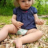 baby, barefoot, blonde_hair, child, curious, diaper, eyes, face, forest, greenery, nature, outdoor, pebbles, polka_dot_dress, portrait, rocks, sitting, toddler, trees, woodland