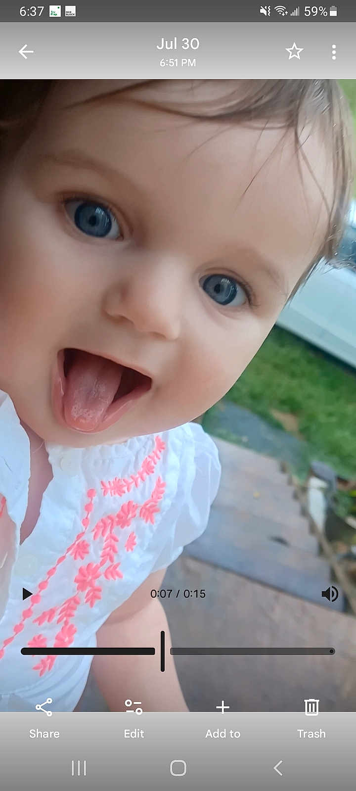 Wednesday is registered to the contest to win money with this photo: baby, child, face, blue_eyes, tongue_out, white_shirt, embroidered_clothing, outdoor, patio, greenery, car, closeup, cute, playful, person, infant, smiling, young_child, headshot, daylight