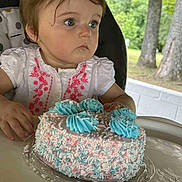 Wednesday joined the competition — help win amazing prizes! birthday, blue_frosting, cake, celebration, child, curly_hair, face, food, grass, hands, high_chair, outdoor, person, pink_embroidery, plate, sprinkles, table, toddler, trees, white_shirt