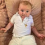 baby, child, infant, white_clothing, polo_shirt, gold_necklace, plush_blanket, decorative_pillow, couch, smiling, cute, portrait, indoors, relaxed, happy, person, young_child, sitting, skin, face