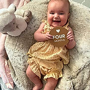 Gabriella joined the competition — help win amazing prizes! baby, infant, smiling, yellow_outfit, plush_toy, cushion, blanket, sign, four_months, happy, cute, indoor, soft_texture, child, person, portrait, lying_down, furniture, head, hands