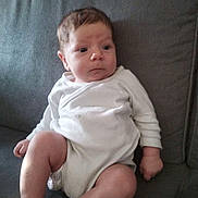 Lylio a rejoint le concours — aidez-le/la à gagner de superbes lots ! baby, infant, child, couch, sofa, white_clothing, onesie, indoor, furniture, sitting, legs, feet, face, hair, skin, looking_away, home, cozy, expression, cute
