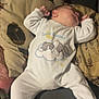 baby, sleeping, onesie, couch, pillow, animal_print, infant, cozy, relaxed, face, clothing, furniture, child, cute, indoor, resting, peaceful, toddler, person, soft