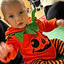 Albie is registered to the contest to win money with this photo: baby, black_stripes, carpet, child, clothing, costume, cute, face, festive, floor, green_leaves, halloween, indoor, motion_blur, orange_clothing, person, pumpkin_costume, sitting, stroller, toddler