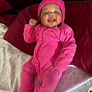 Liana joined the competition — help win amazing prizes! baby, pink_onesie, knitted_hat, smiling, lying_down, bed, pillow, blanket, happy, infant, child, cute, portrait, indoors, fabric, cozy, warm_clothing, human, face, one_person