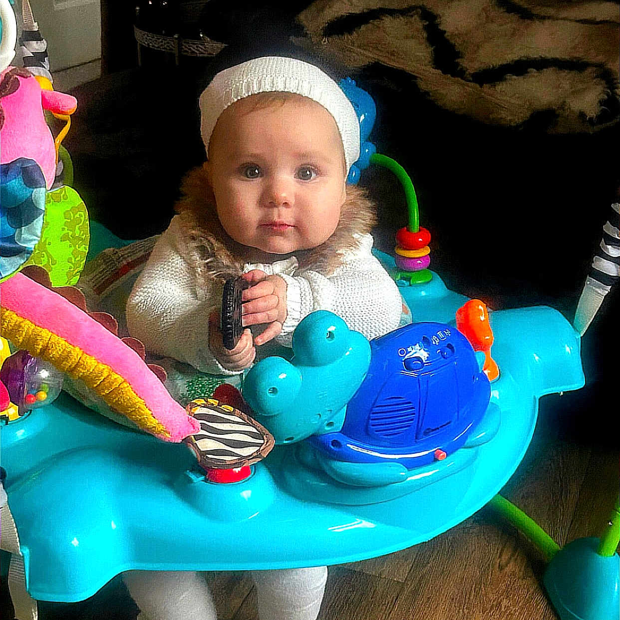 Marlie joined the competition — help win amazing prizes! activity_center, baby, blanket, blue, child, colorful, curious, cute, floor, furniture, home, indoor, infant, knit_hat, person, playful, sitting, toy, white_clothing, wood_floor
