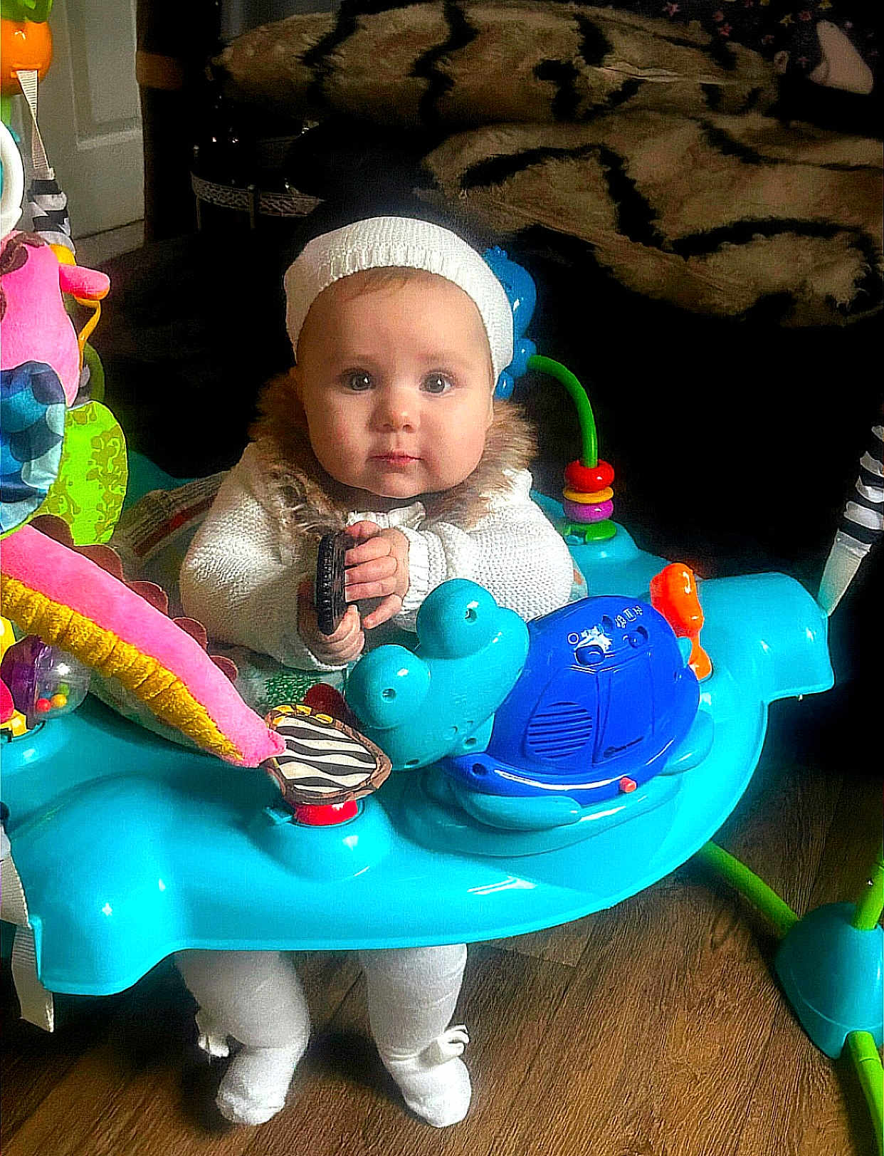 Marlie joined the competition — help win amazing prizes! baby, child, infant, activity_center, toy, blue, white_clothing, knit_hat, floor, wood_floor, indoor, cute, curious, sitting, furniture, blanket, colorful, playful, person, home