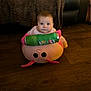baby, child, floor, plush_toy, snack_can, pringles, wooden_floor, pink, curious, indoors, furniture, couch, blanket, sitting, face, person, home, cozy, young_child, toy